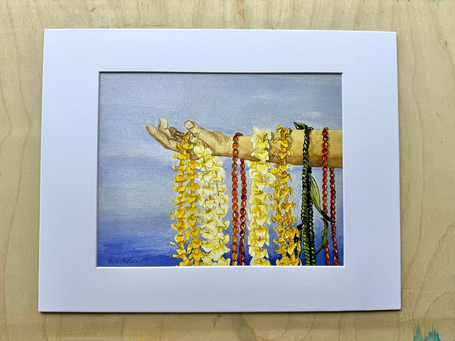 Watercolor of hand holding Puakenikeni lei, Plumeria lei, Wiliwili lei, and ti leaf lei with blue background art print in a white mat.
